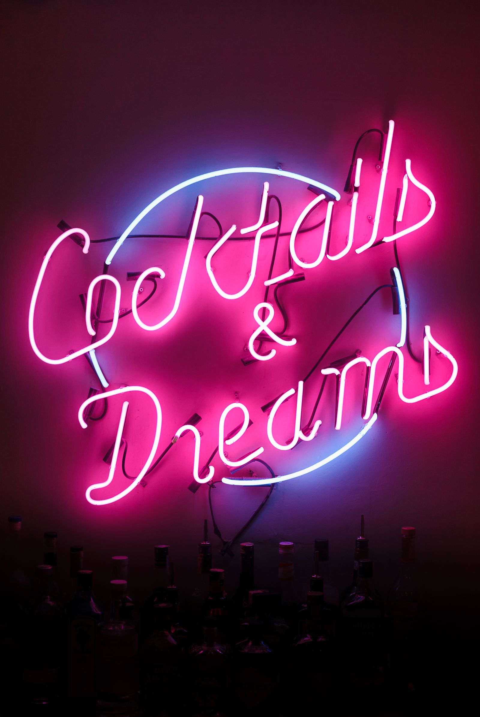 Enseigne néon rose « Cocktails & Dreams » au-dessus de bouteilles dans un bar